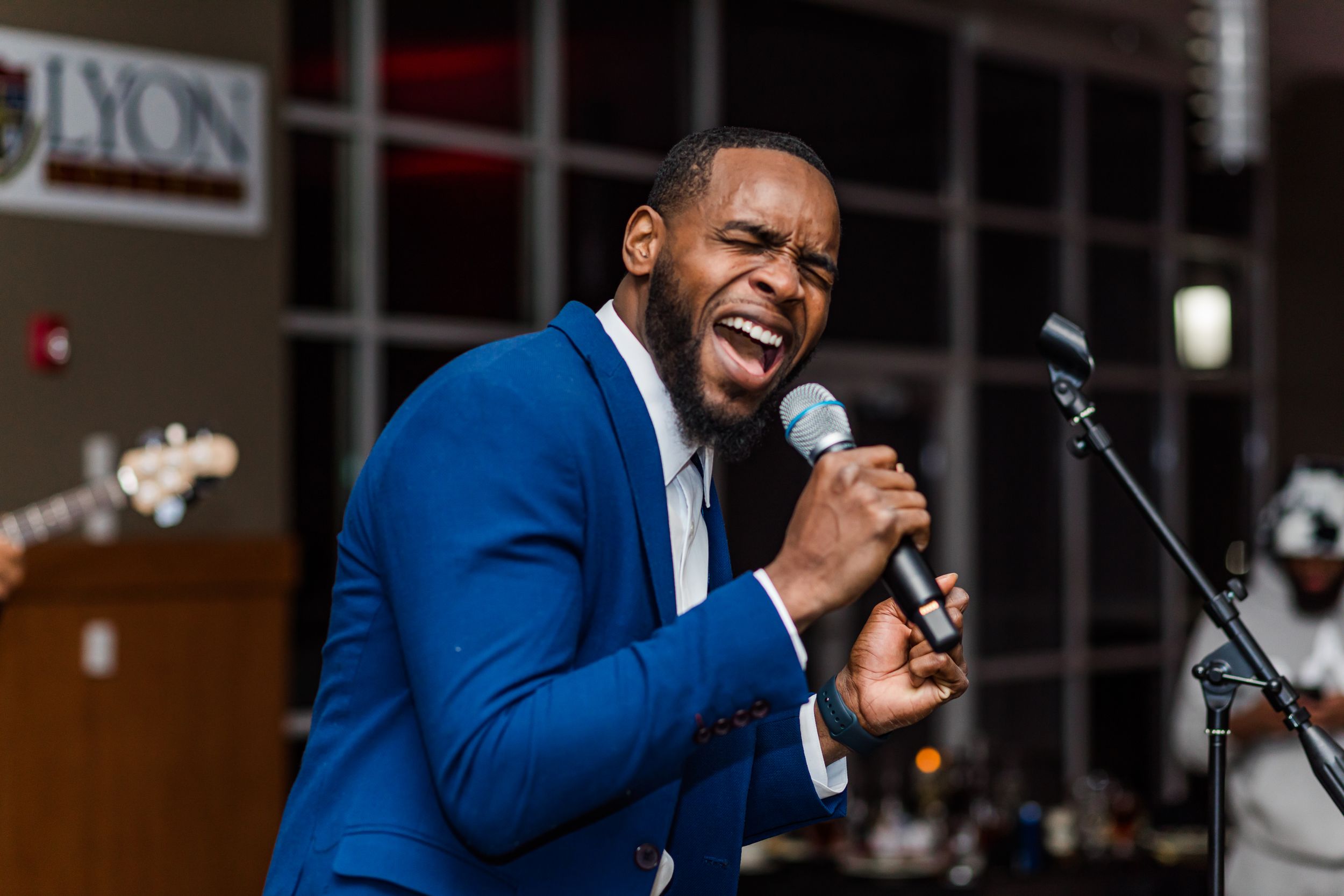 An entertainer in a blue suit singing passionately into a microphone during a performance.