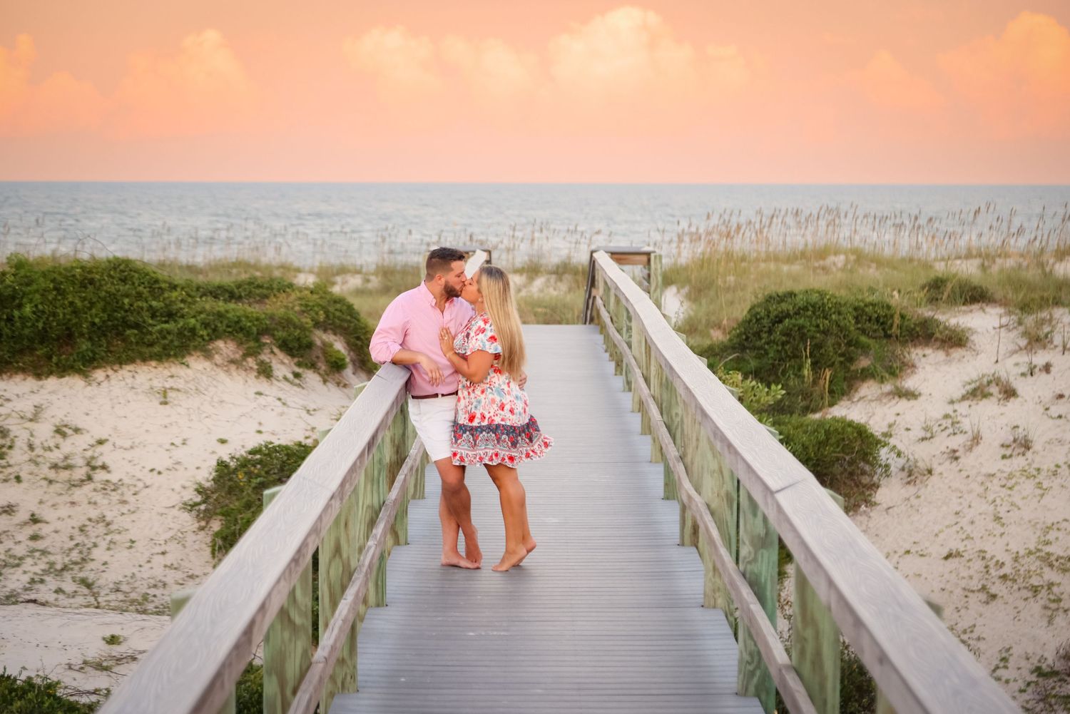 A couple shares an intimate moment on a wooden boardwalk at sunset by the beach.