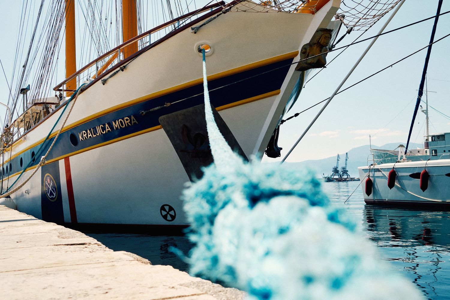 Large sailing yacht moored at dock with blue rope in foreground.
