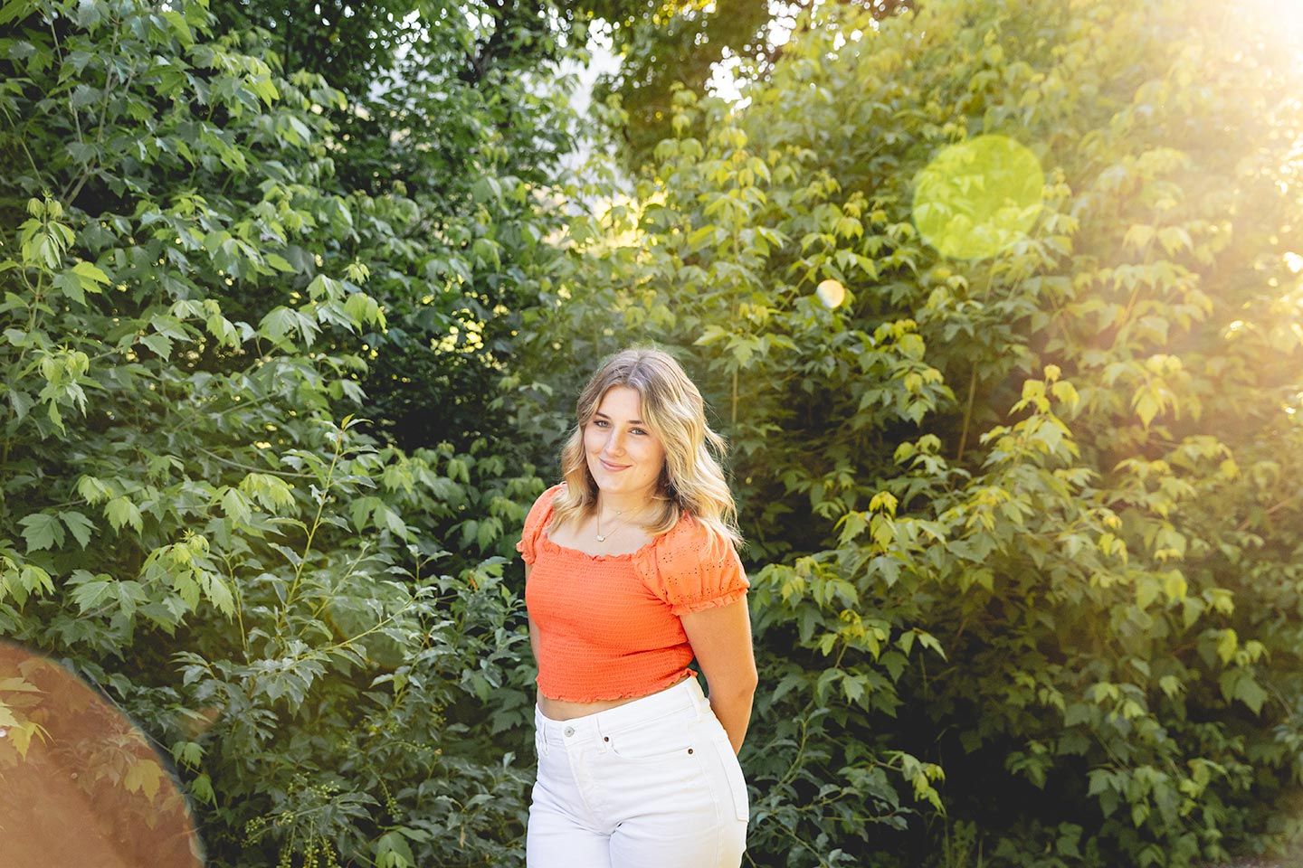 Senior girl posing for her high school professional photos.  Standing in front of greenery