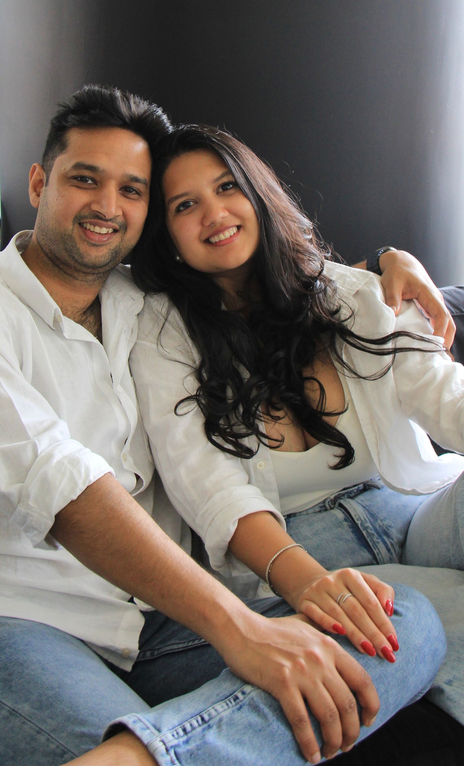 A couple wearing matching white shirts smile warmly while sitting close together on a couch.