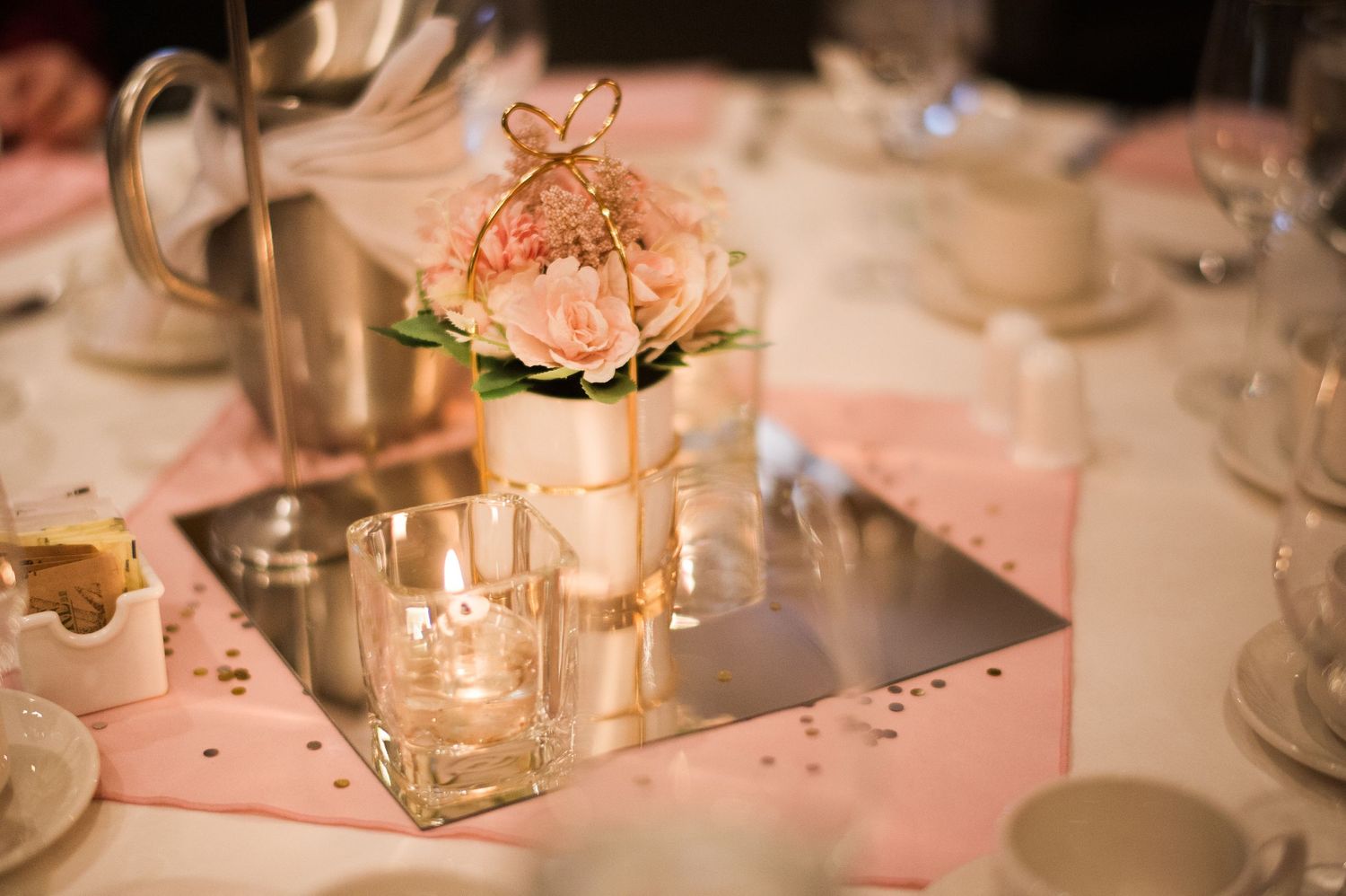 Elegant wedding centerpiece with delicate pink flowers in a glass vase surrounded by candlelight.