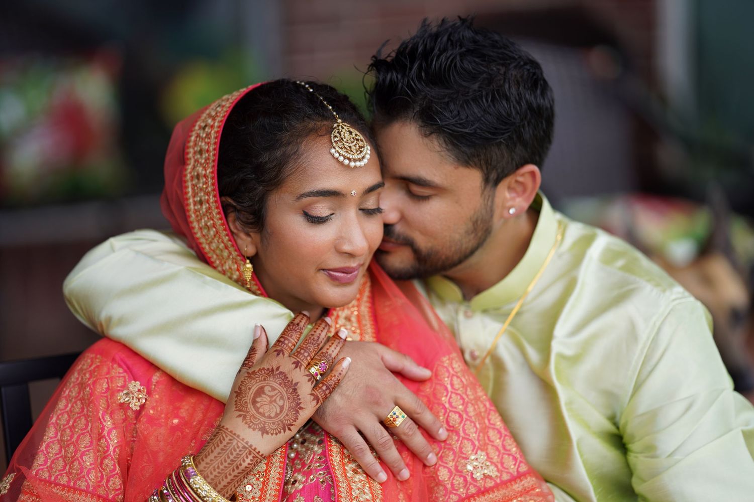 A romantic moment between a couple in traditional Indian wedding attire with the bride in red and groom in cream.