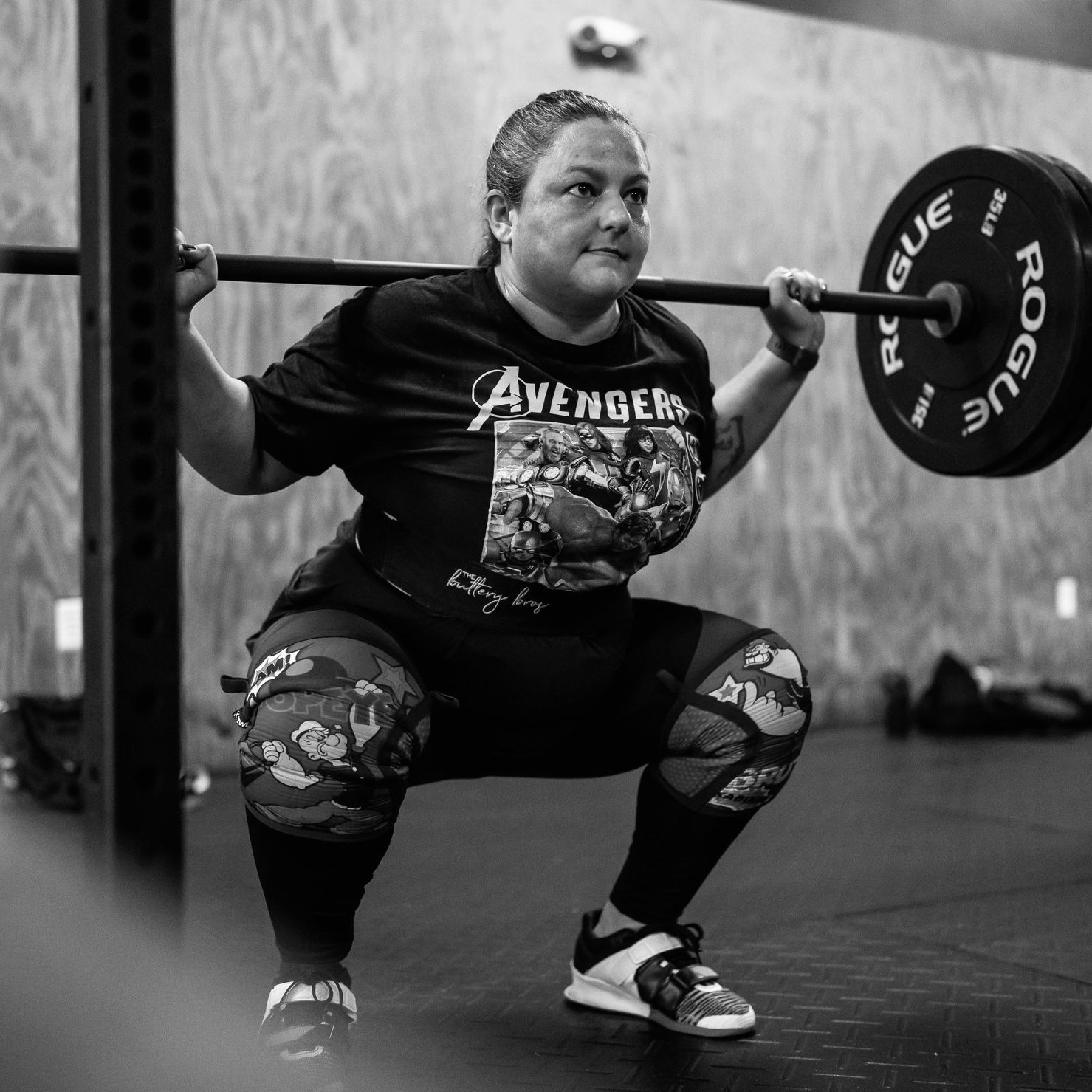 Weightlifter in Avengers shirt performing a deep squat with barbell in a gym setting.
