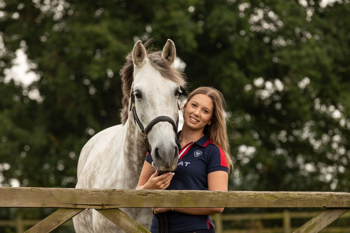 A white horse receives affection while standing at a wooden fence.