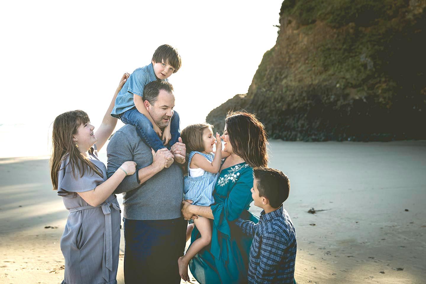 family together at the beach with toddler on dad's shoulders and mom holding little daughter and big kids hugging parent