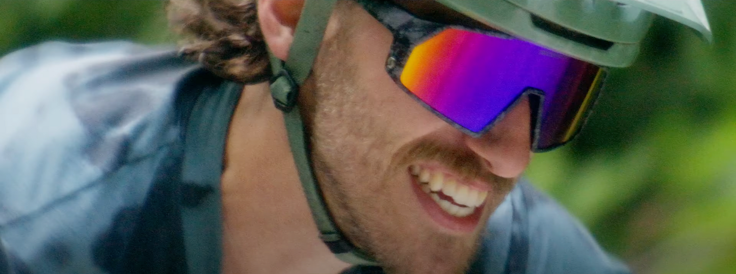 Cyclist wearing blue jacket and reflective sports sunglasses during outdoor activity.