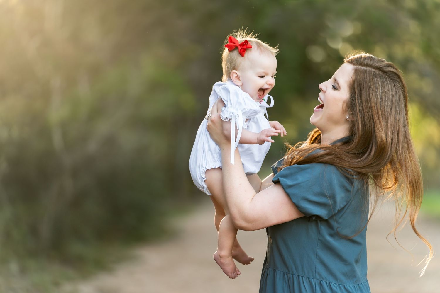 mother wearing a green dress lifts her infant daughter up and looks at her as they both laugh