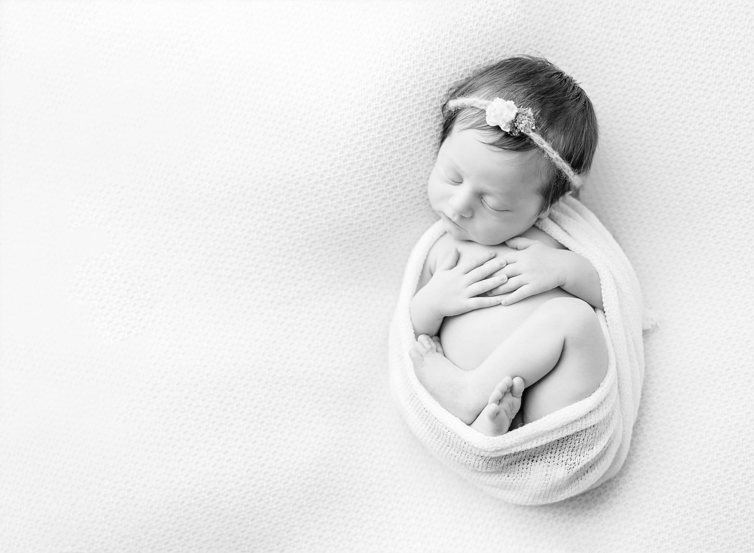 Black and white portrait of sleeping newborn wrapped in soft fabric.