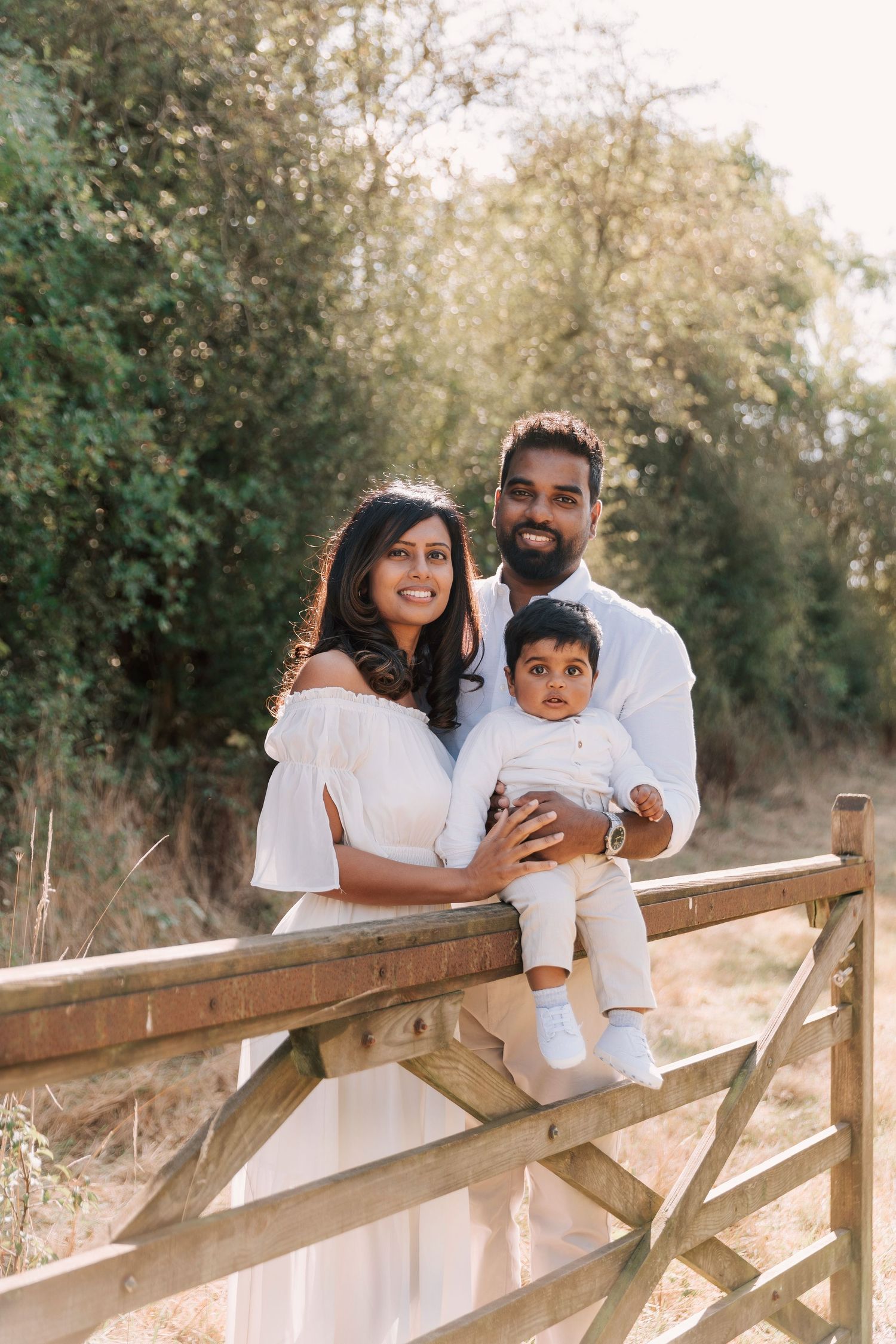 Family in white outfits poses together on wooden fence in natural outdoor setting.