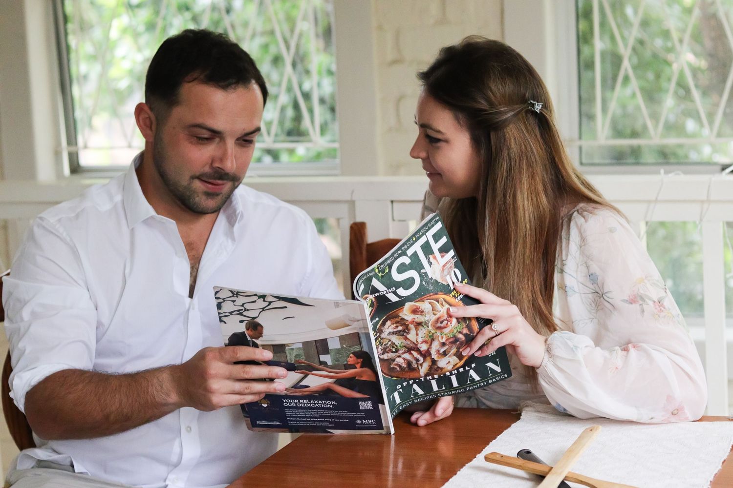 Two people reviewing a photo book together at a sunlit table indoors.