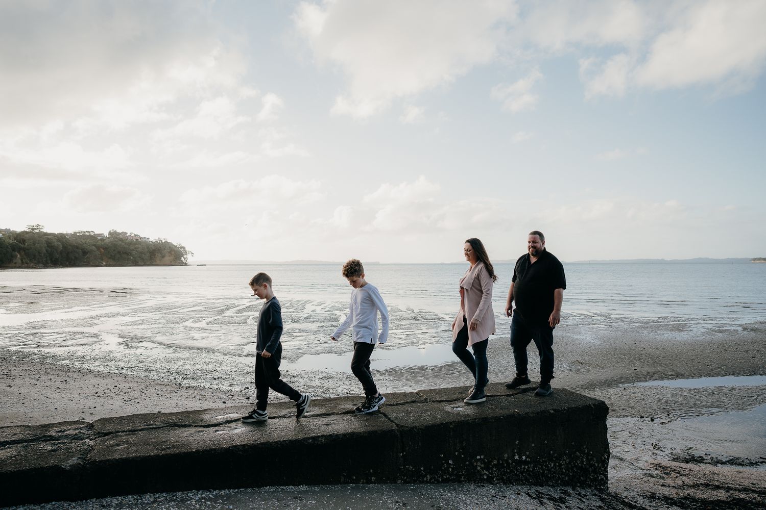 family of four walk along a concrete pipe at cockle bay beach