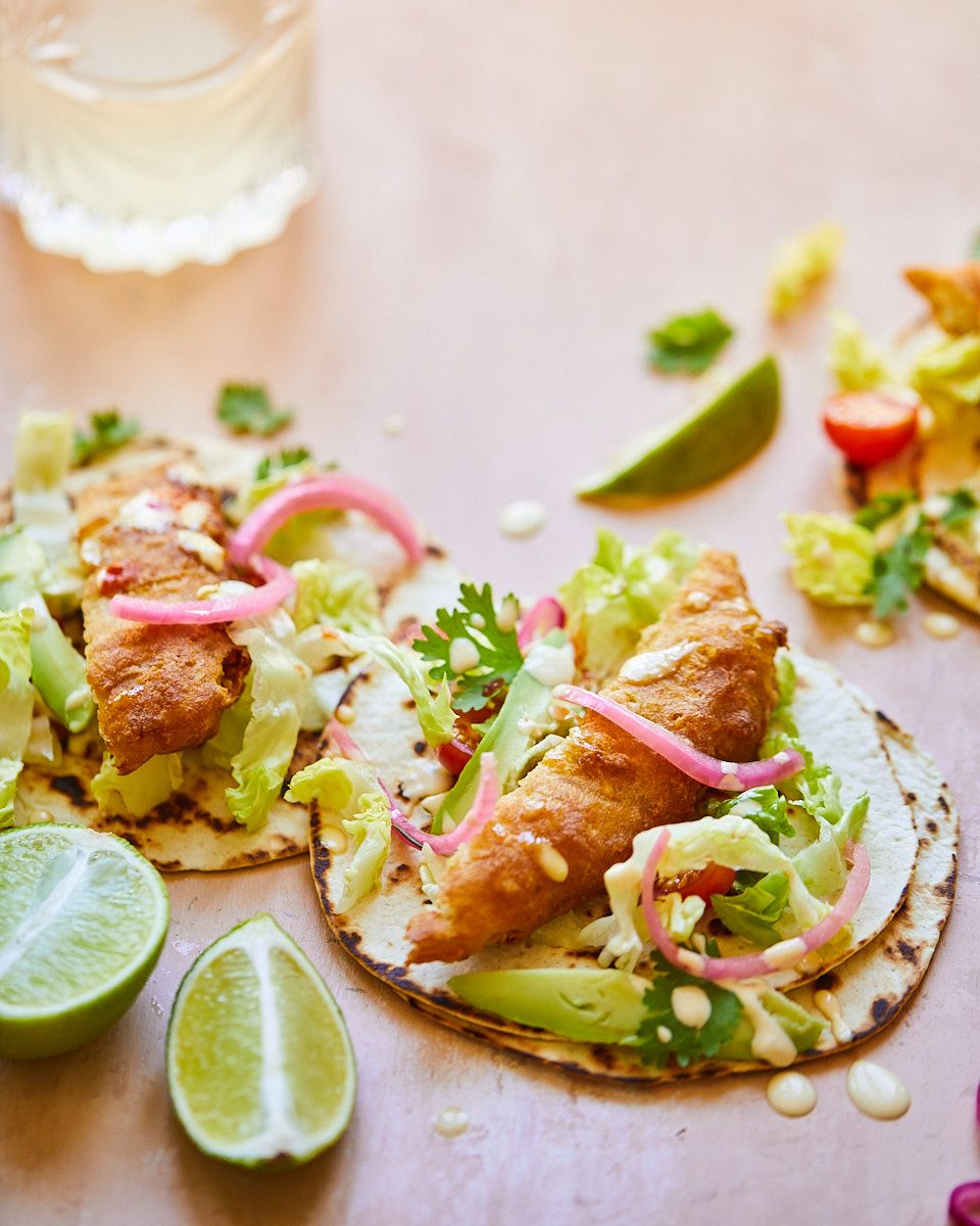 Fish tacos topped with shredded lettuce, pickled onions and lime wedges.
