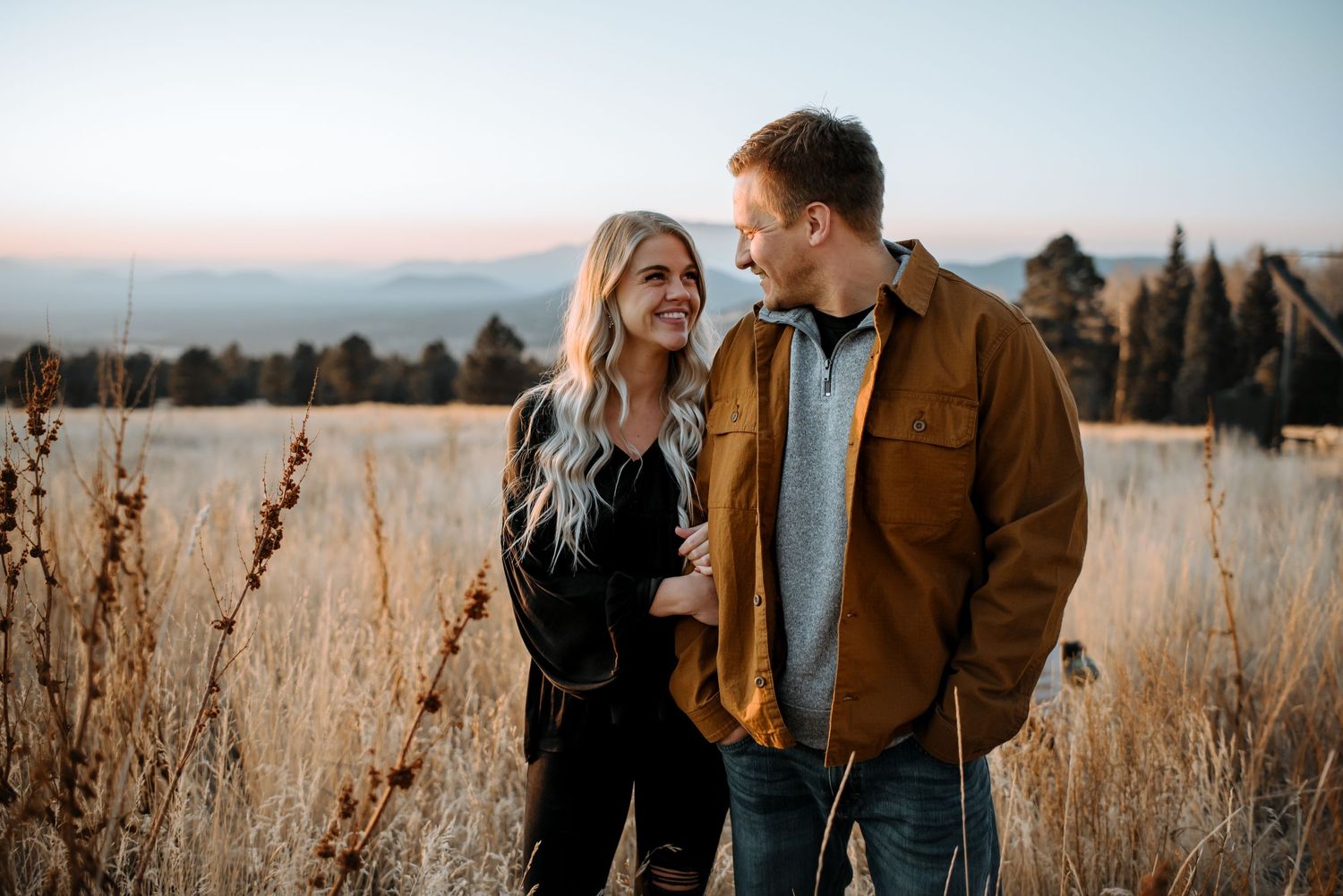 Couple walking through golden field at sunset wearing casual attire.