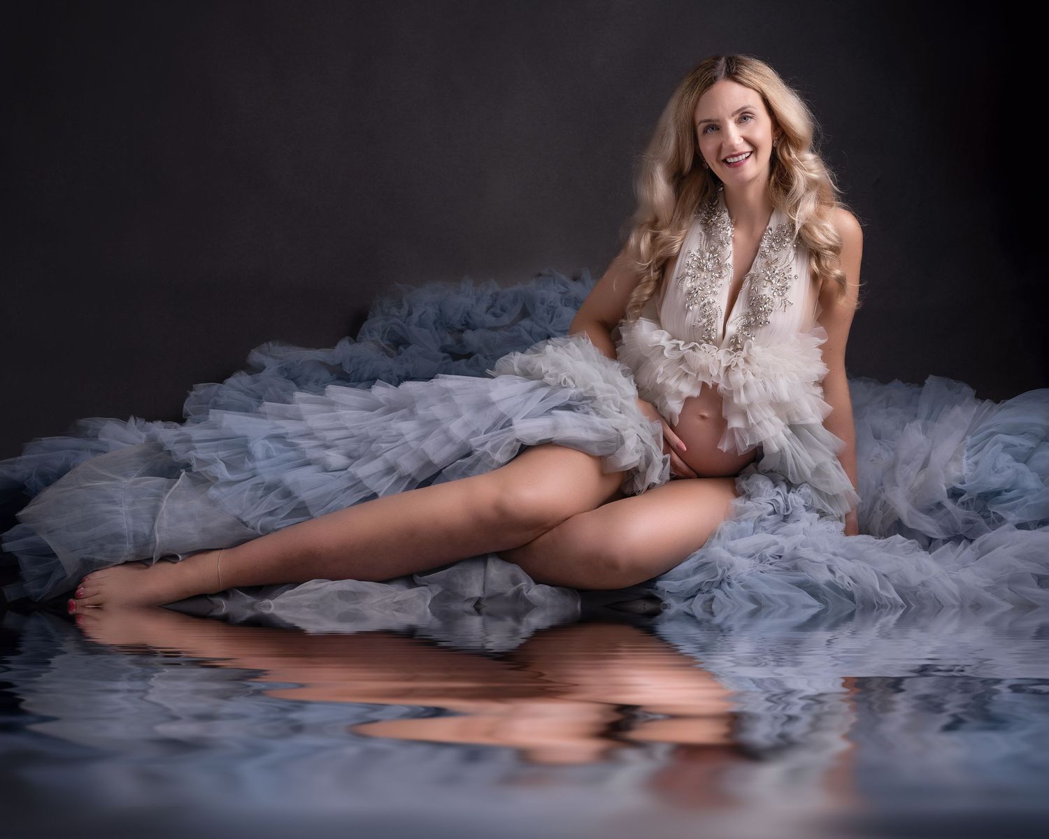 Artistic portrait featuring flowing blue tulle fabric and dramatic lighting on a dark background.