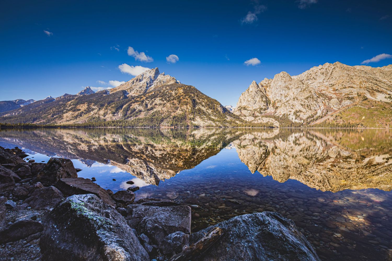 Majestic mountain peaks reflecting perfectly in a crystal-clear alpine lake under blue skies.