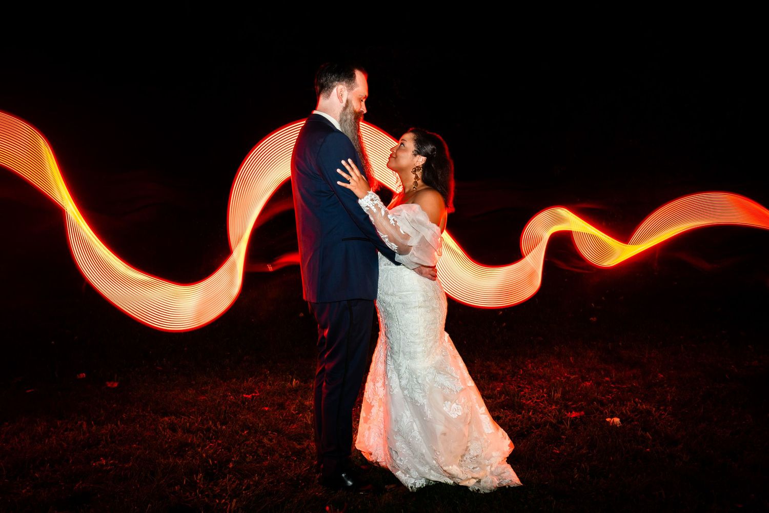 Long exposure light painting creates glowing orange trails around a couple in formal attire.