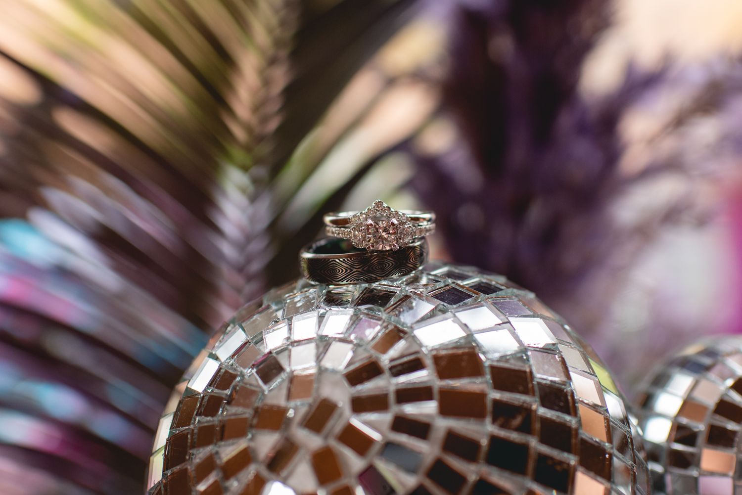 Diamond engagement ring displayed on a reflective disco ball surface with colorful lighting.