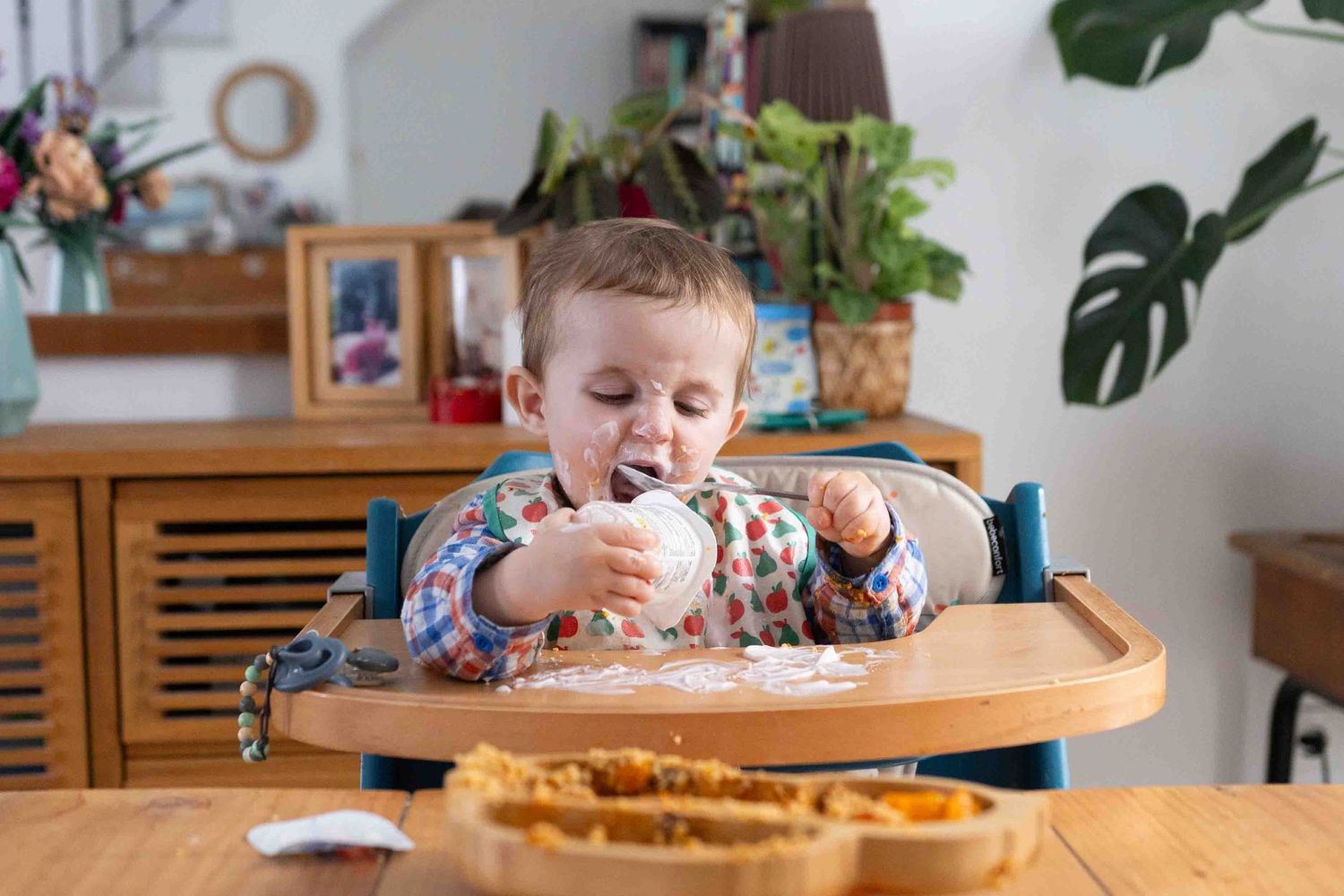 Young child in high chair enjoying a snack or meal at wooden dining table.
