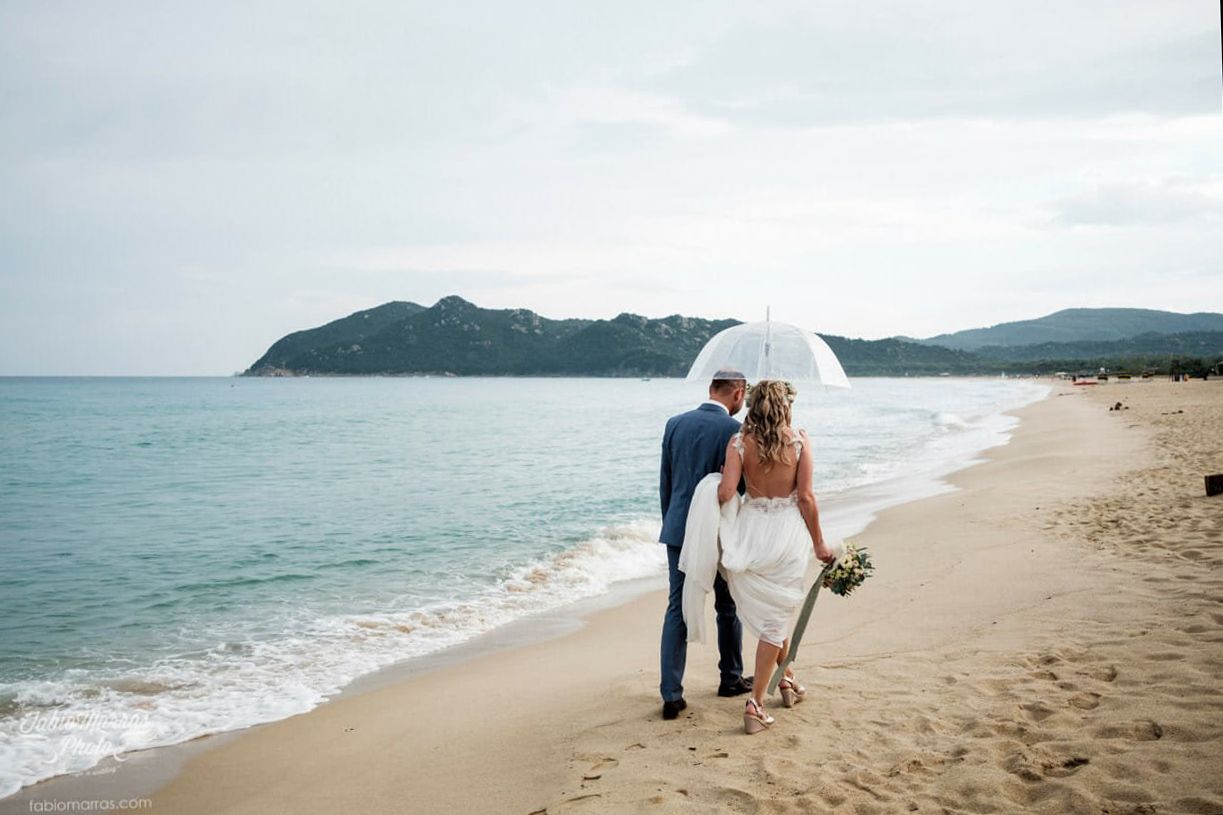 Ein entspanntes Paar lacht unter einem Regenschirm am Strand – Natürliche Hochzeitsfotografie, die echte Emotionen über die perfekte Inszeni