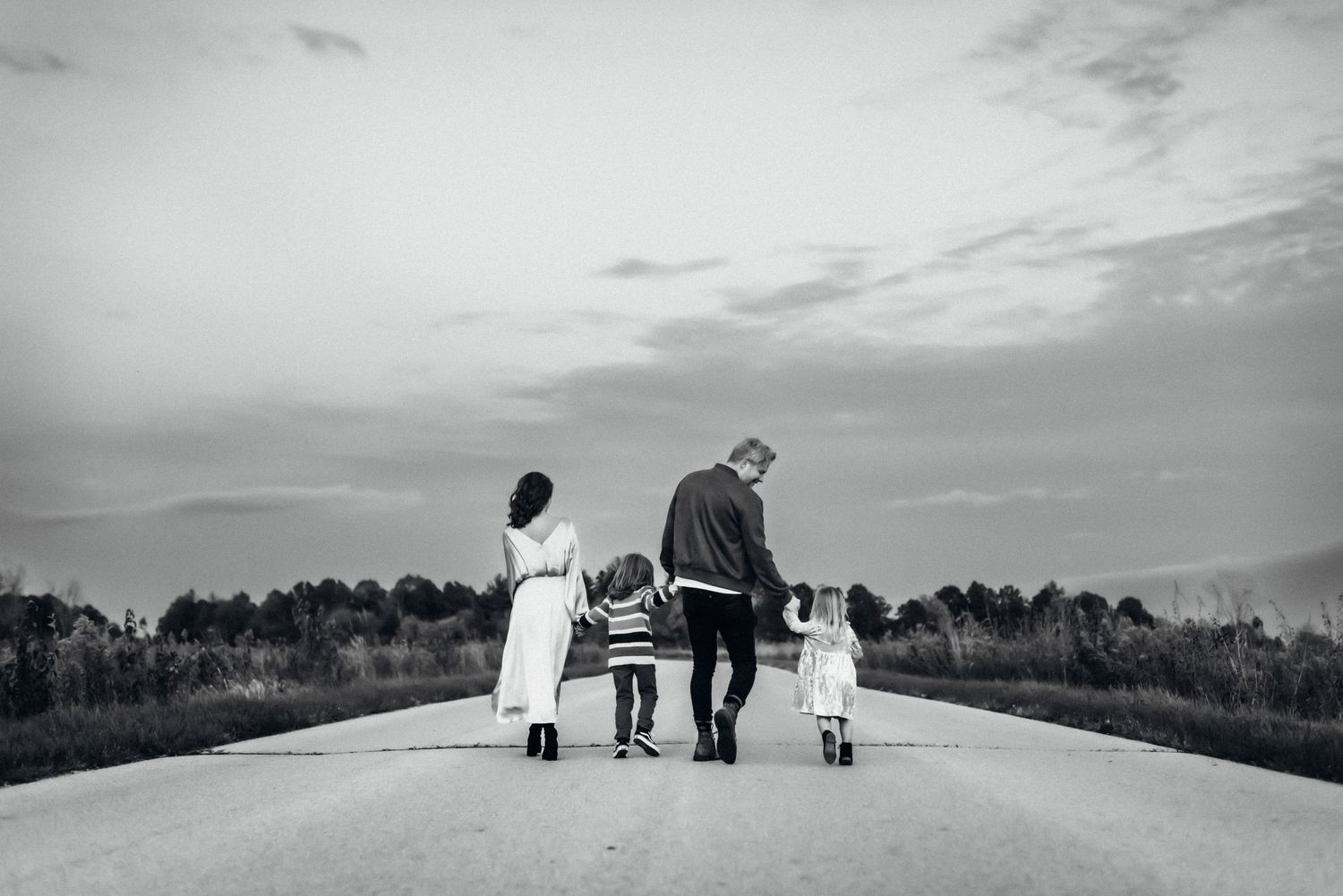 A family walking together holding hands on an empty road against a cloudy sky.