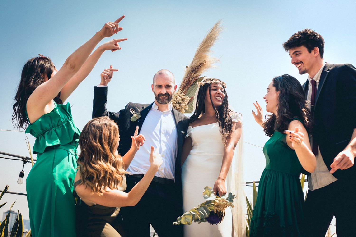 Lively wedding party celebration with bridesmaids in green and groomsmen in black suits outdoors.
