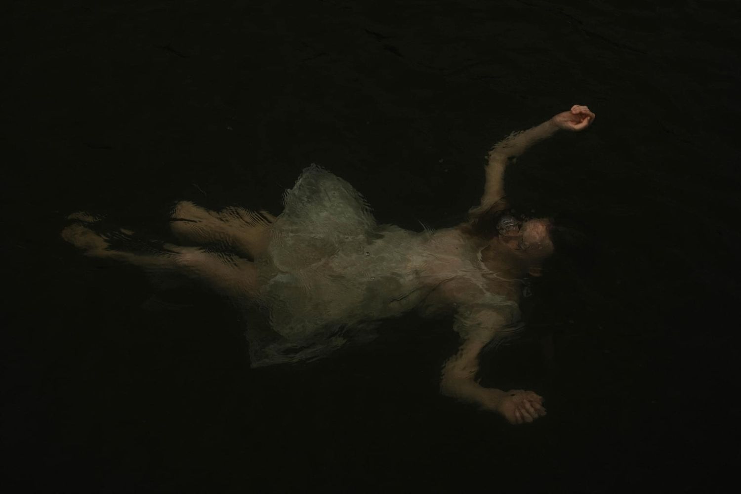 Girl in white dress floating just under the surface of the water in a lake with ripples going out in every direction