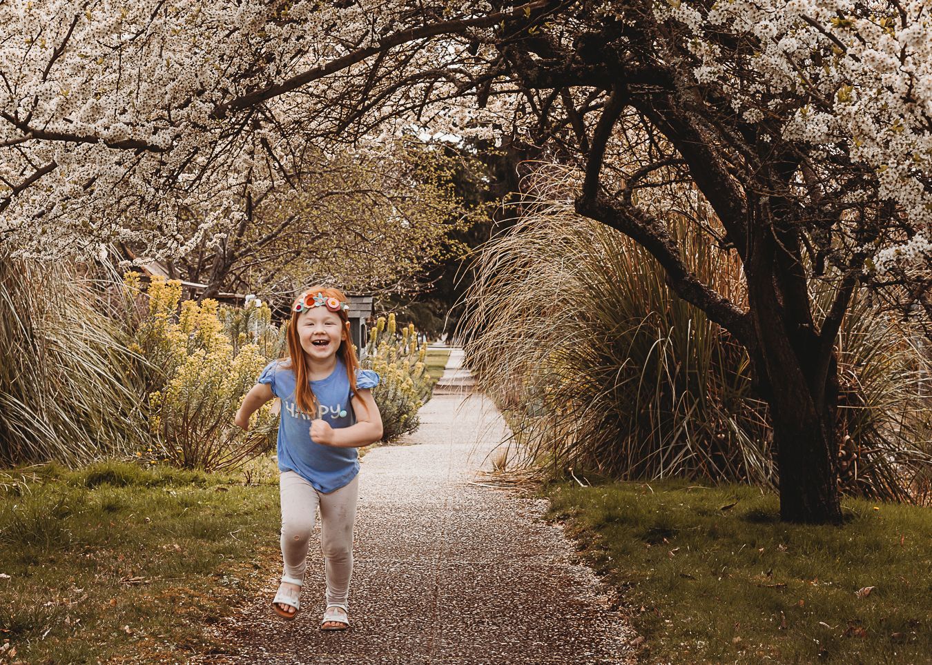Young child runs joyfully down a peaceful path lined with autumn trees and tall grasses.