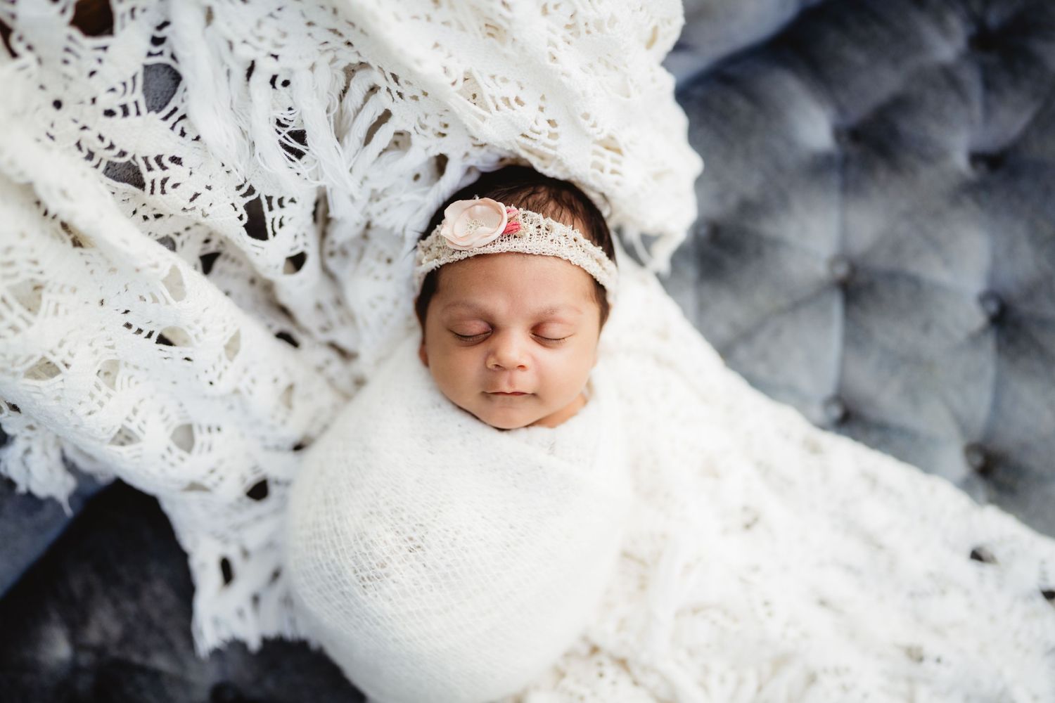 Sleeping newborn wrapped in white against grey textured background with lace details.