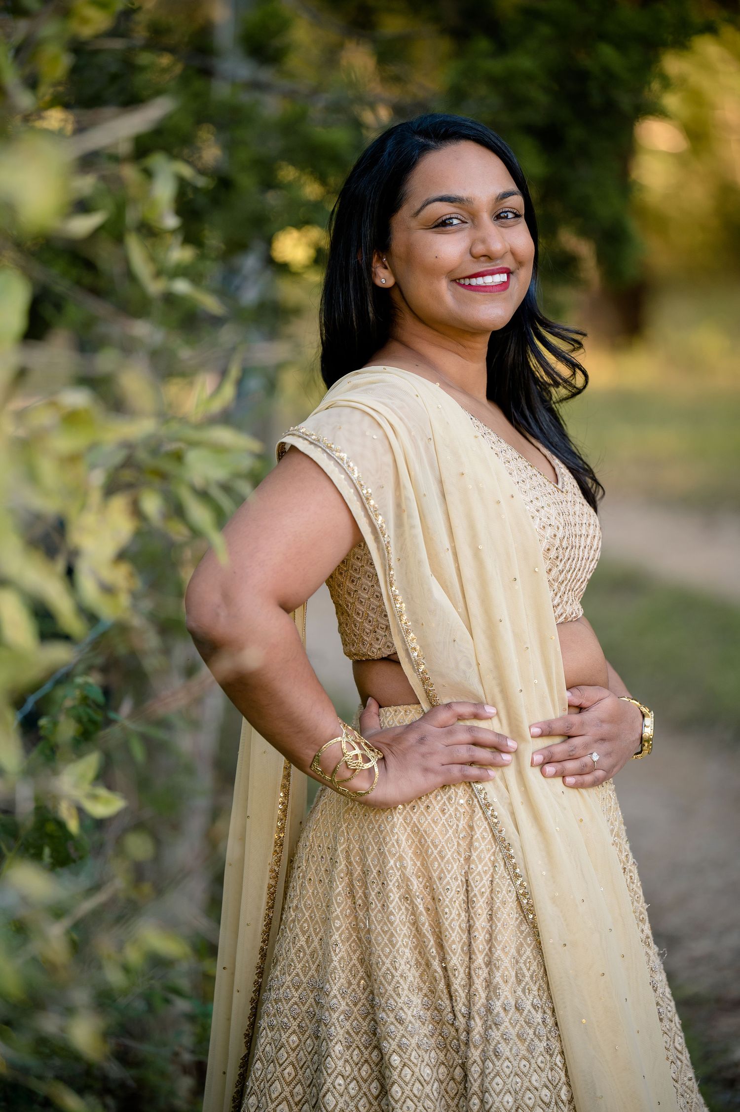 Traditional gold beaded lehenga outfit photographed in outdoor natural setting.