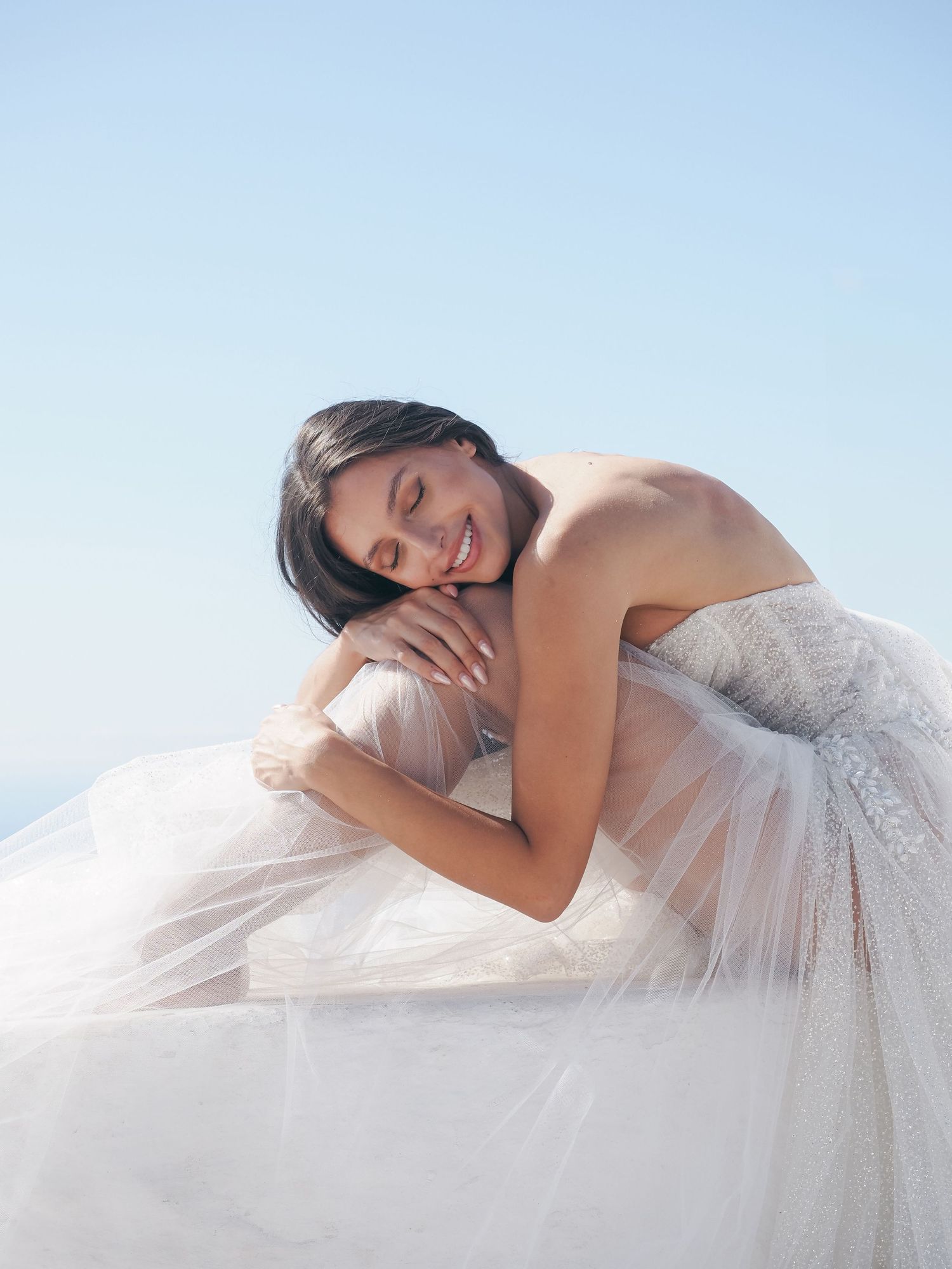 A dreamy bridal portrait featuring a white tulle dress against a bright sky.