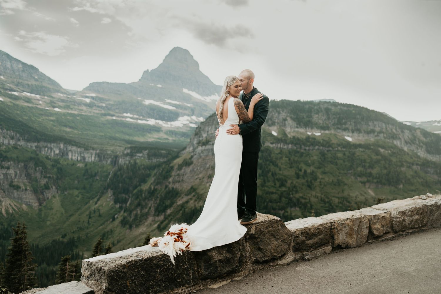 Wedding couple embracing at scenic mountain overlook with dramatic mountain peaks.