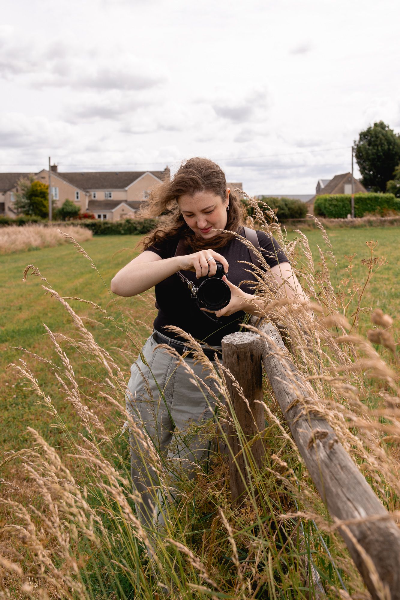 A photographer in black clothing takes photos while lying among wild grasses.