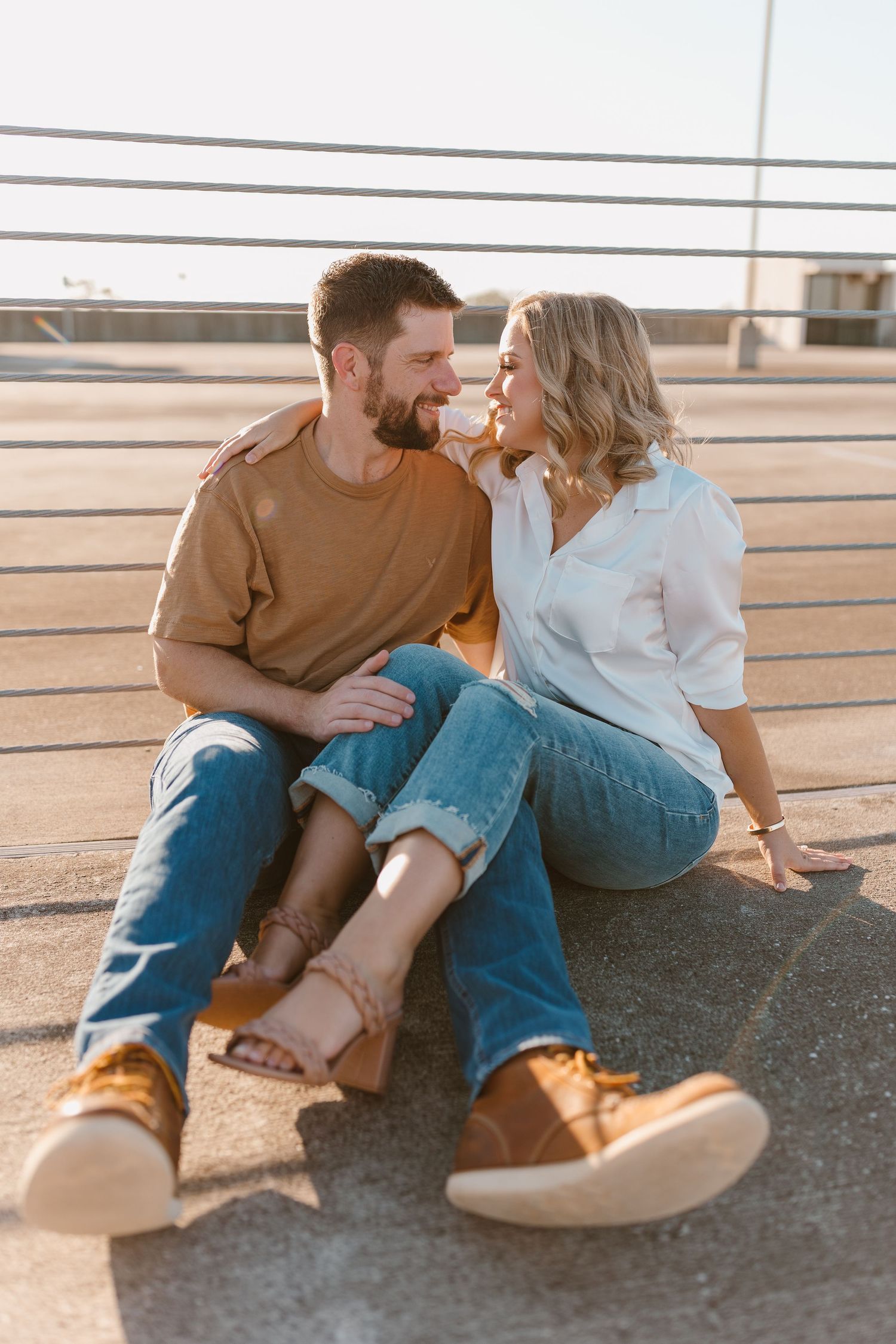 Couple in casual wear sitting together on concrete ground during golden hour.