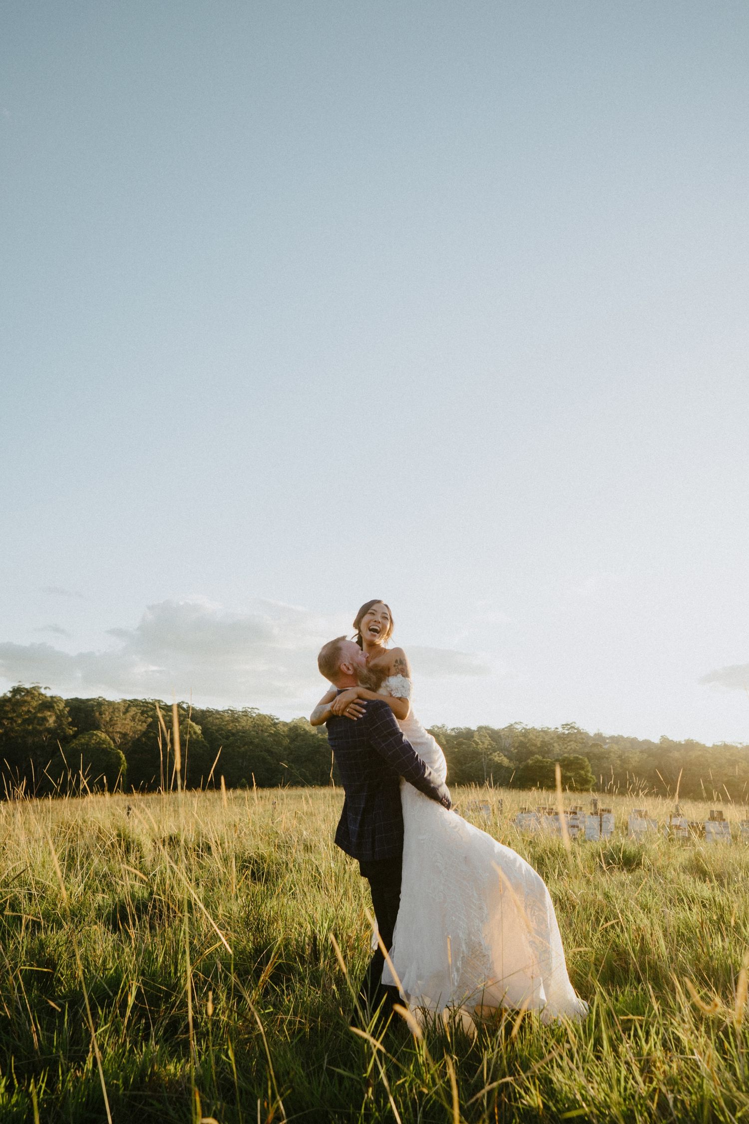 Groom lifting bride in joyous embrace in a sunlit field at Ocean view estates