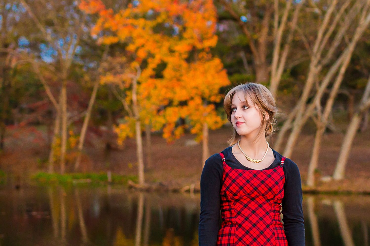 Portrait against vibrant orange fall foliage and reflective pond.