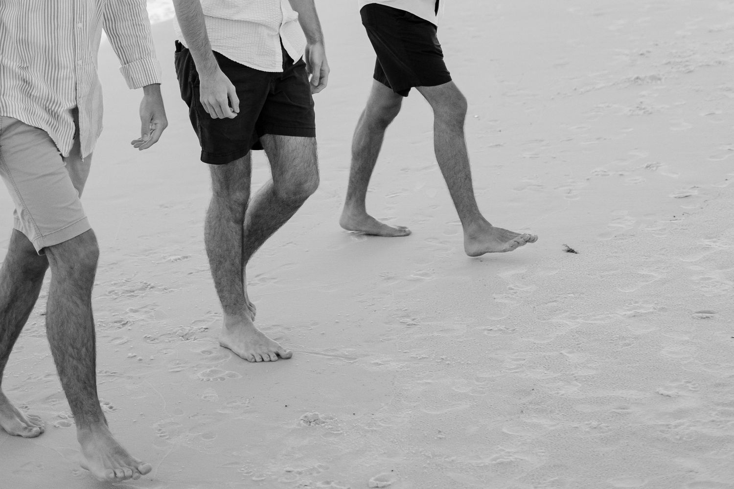 Black and white photograph of people walking on a sandy beach.