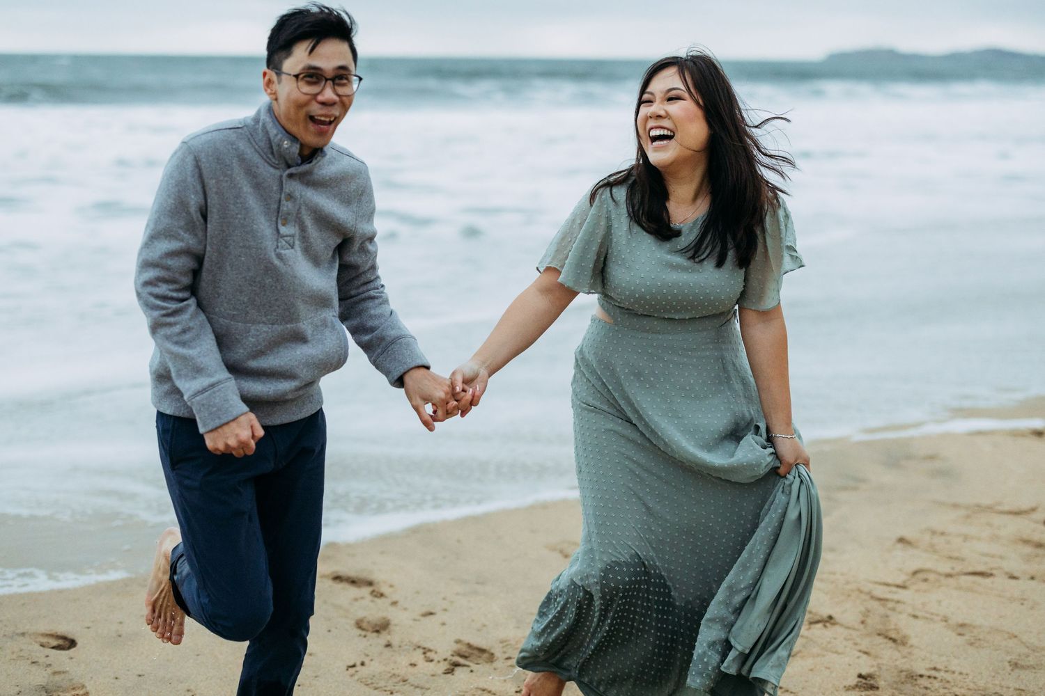Asian couple runs out of Pacific ocean along Half Moon Bay beach.