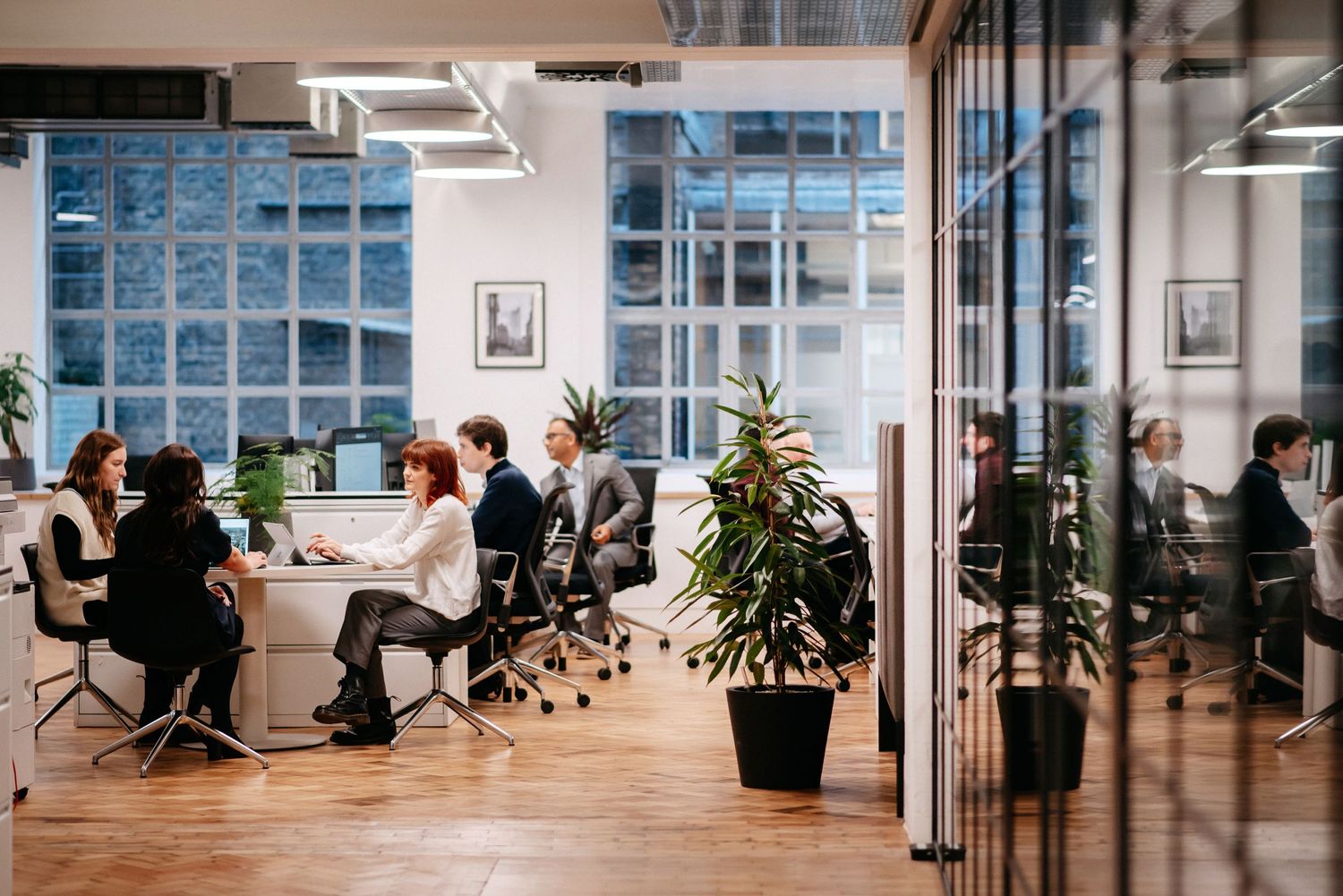 Modern open plan office with glass walls and people working at desks.