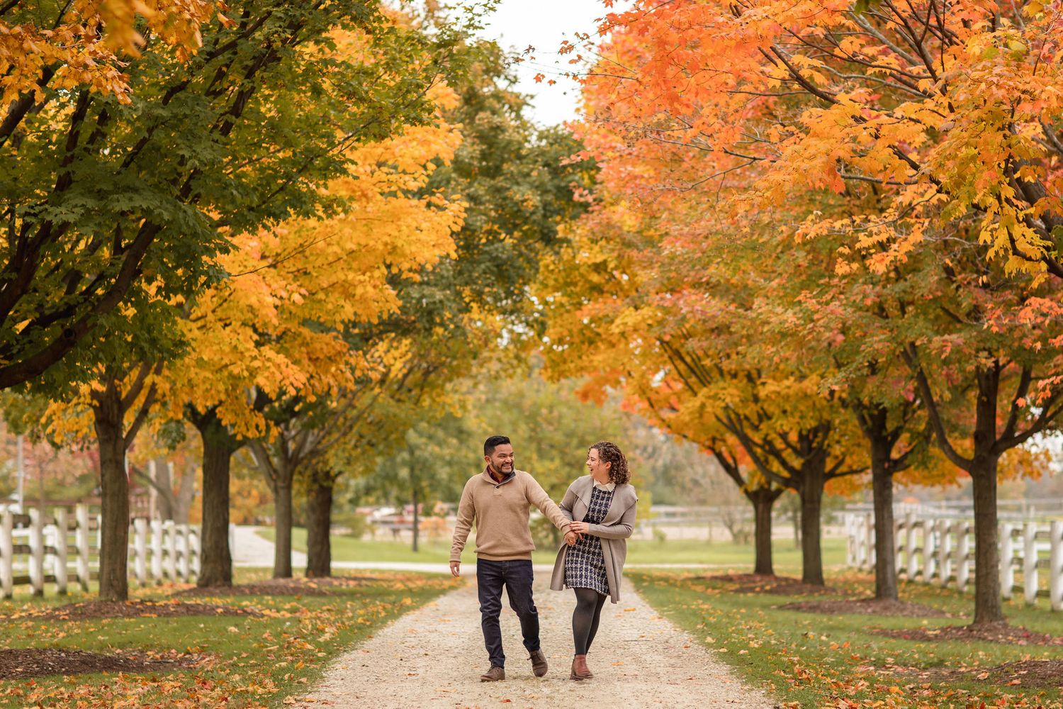 Couple walking on path under vibrant orange and yellow autumn trees.