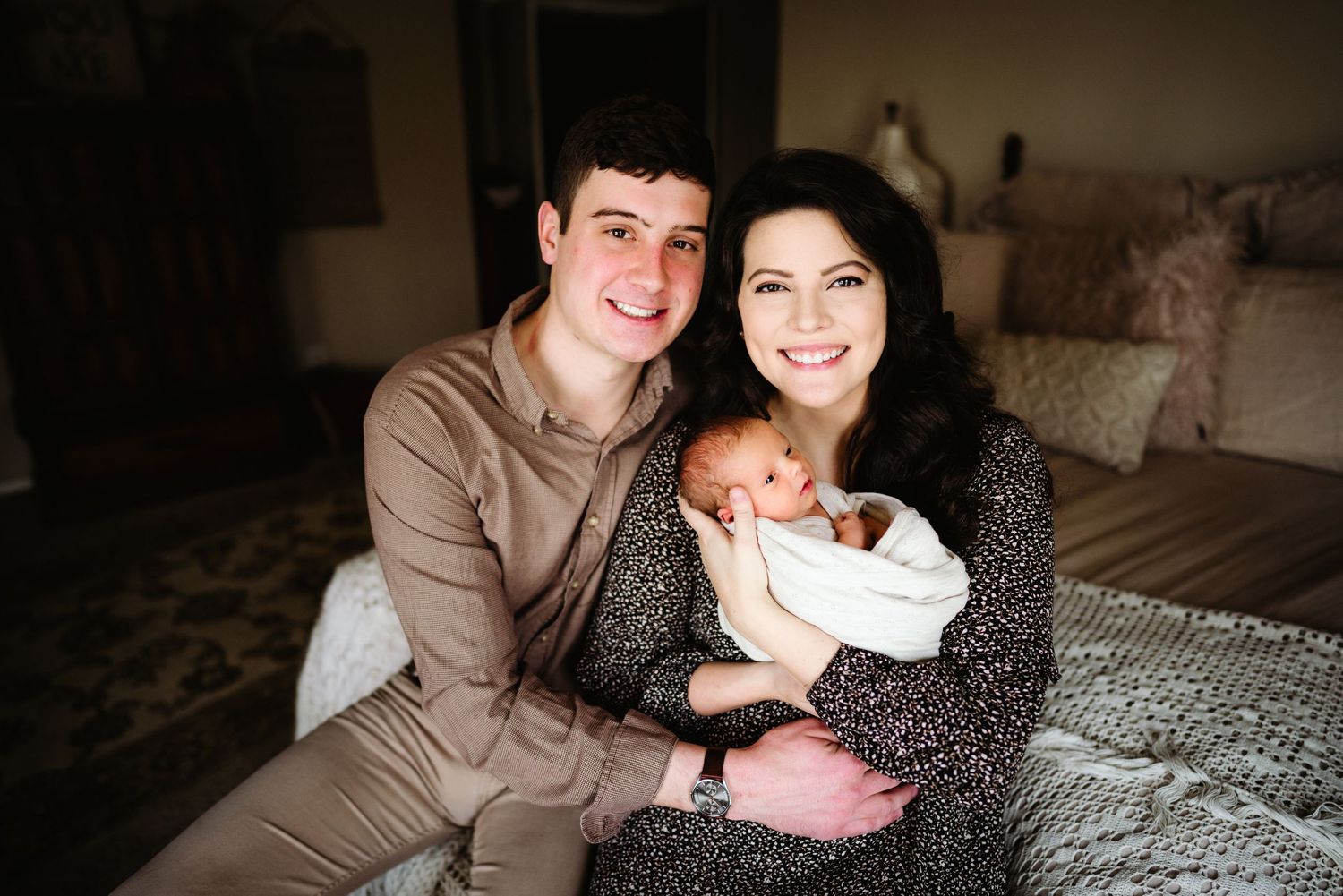 Intimate family portrait with a newborn baby being held lovingly in a dimly lit living room.