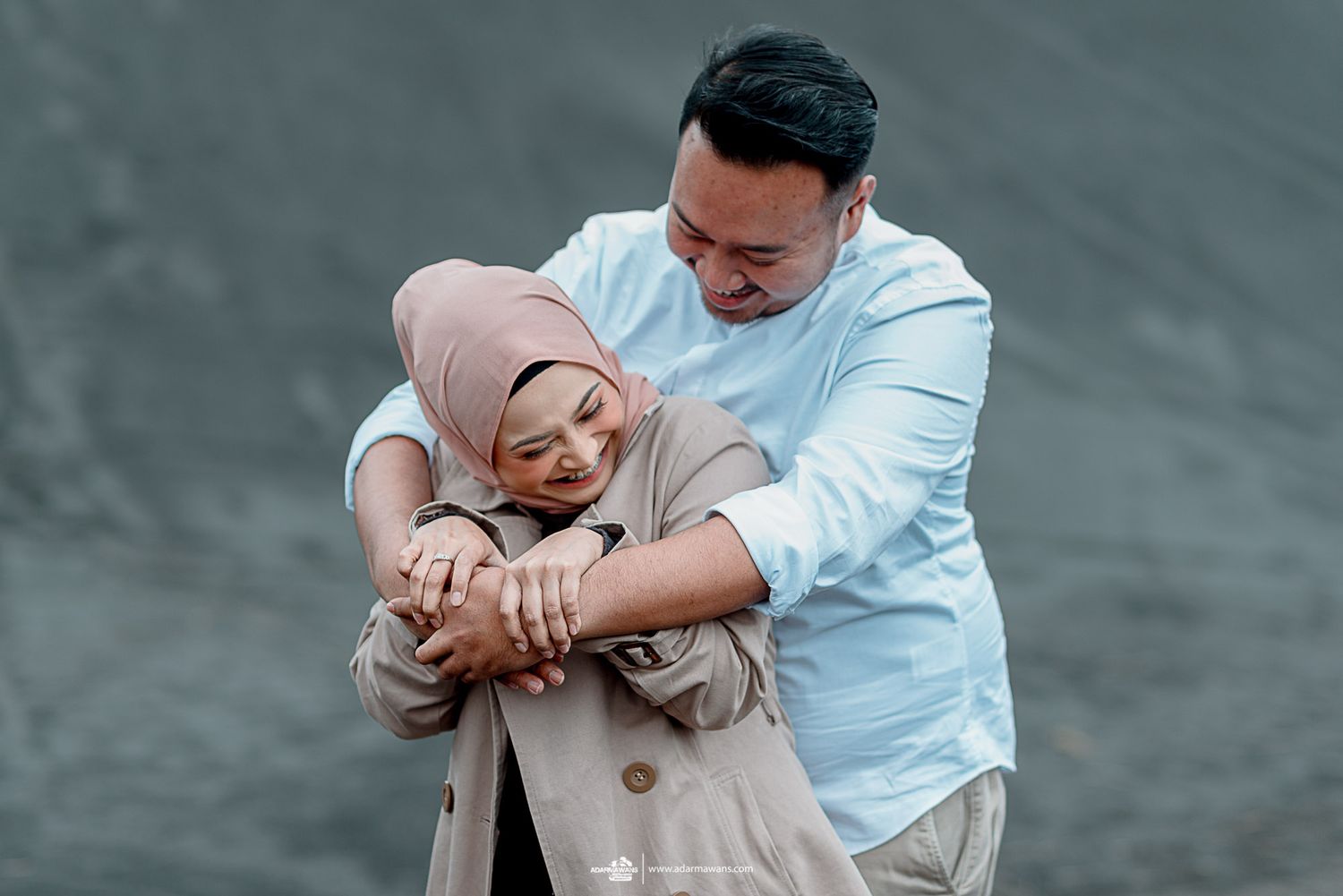 Romantic couple embrace in casual attire during outdoor photoshoot.