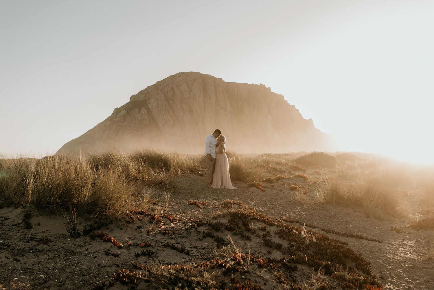 A dreamy silhouette stands on a misty hillside during golden hour with a mountain peak in the background.