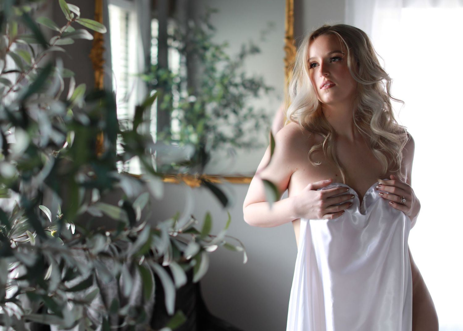 Ethereal boudoir portrait with soft lighting and indoor plants in background.