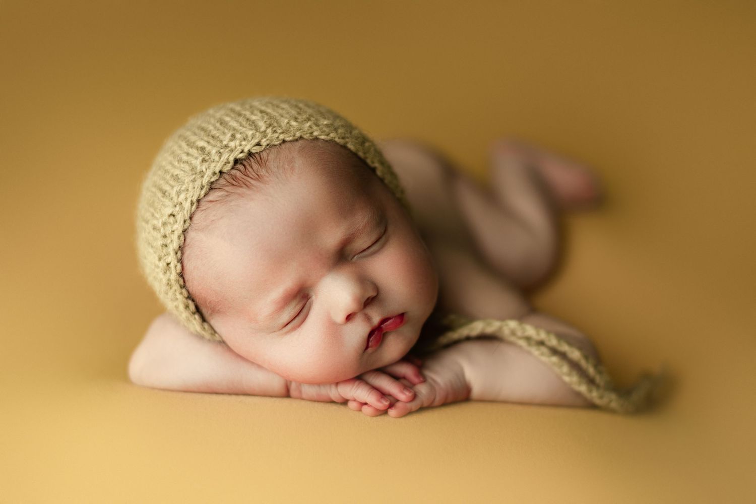 baby boy posed for a newborn photo session with a mustard yellow backdrop