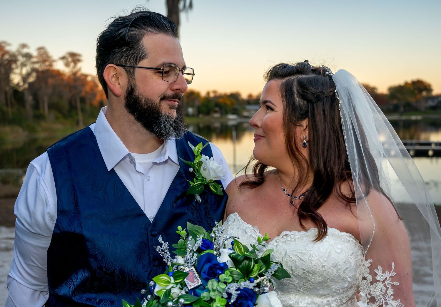 Romantic sunset wedding portraits by a lake with blue florals and natural light.