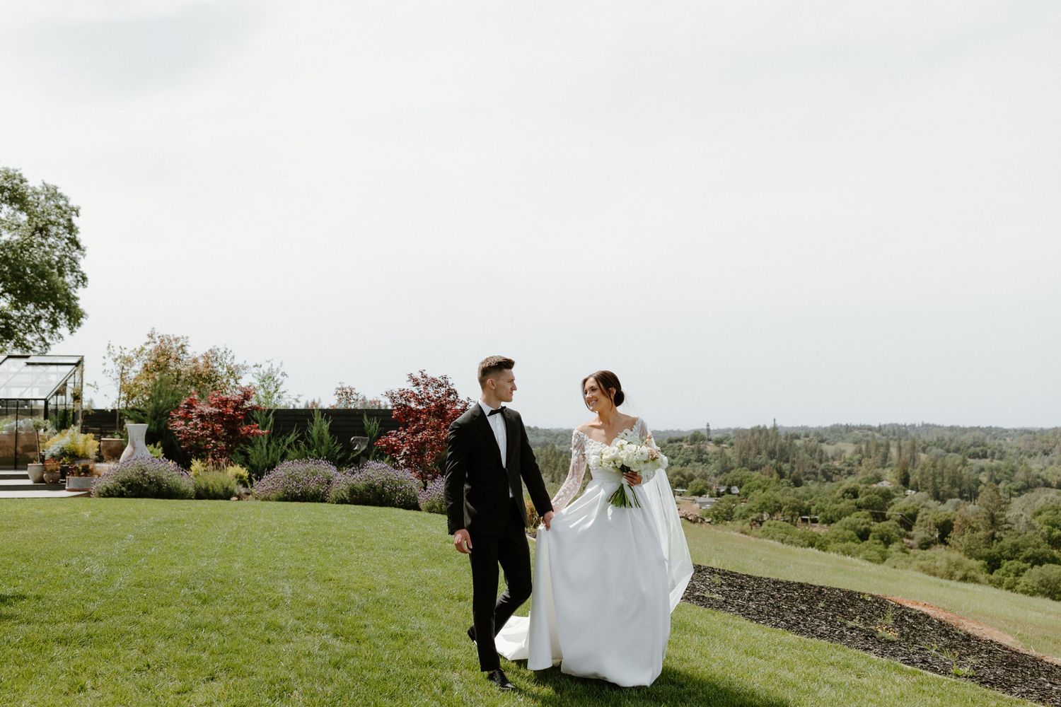A newly married couple walks together on a manicured lawn with scenic views.
