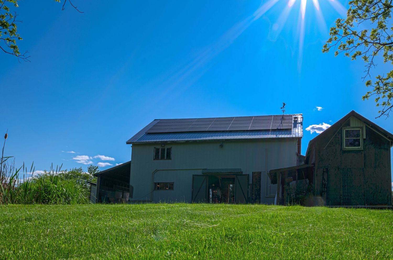 Modern farmhouse with solar panels under bright blue sky and sunburst.