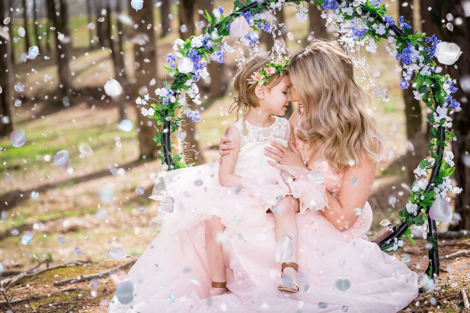 Mother and daughter in matching pink tulle dresses pose beneath a floral arch in a dreamy woodland setting.