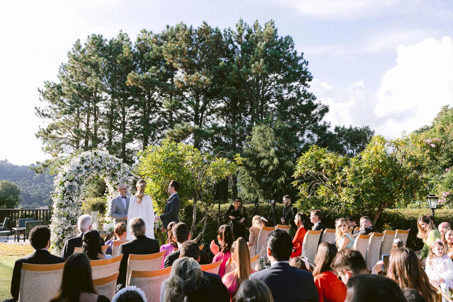 Outdoor wedding ceremony with pine trees backdrop and seated guests in attendance.